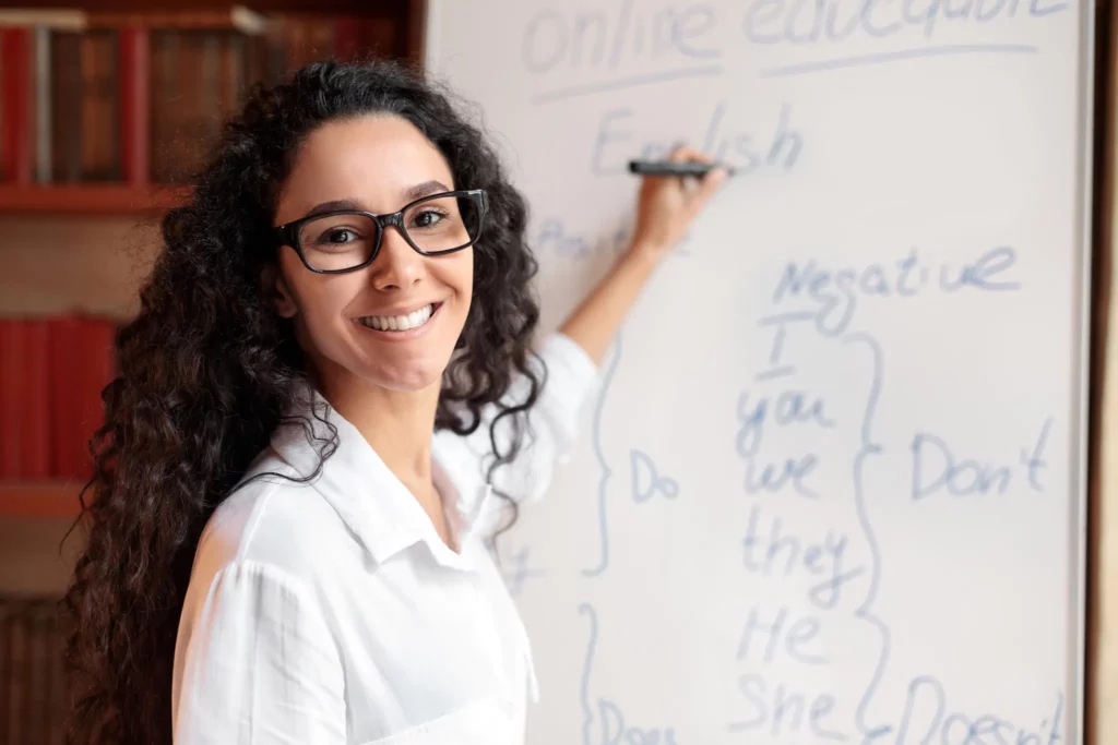 Smiling teacher writing English grammar on whiteboard in classroom