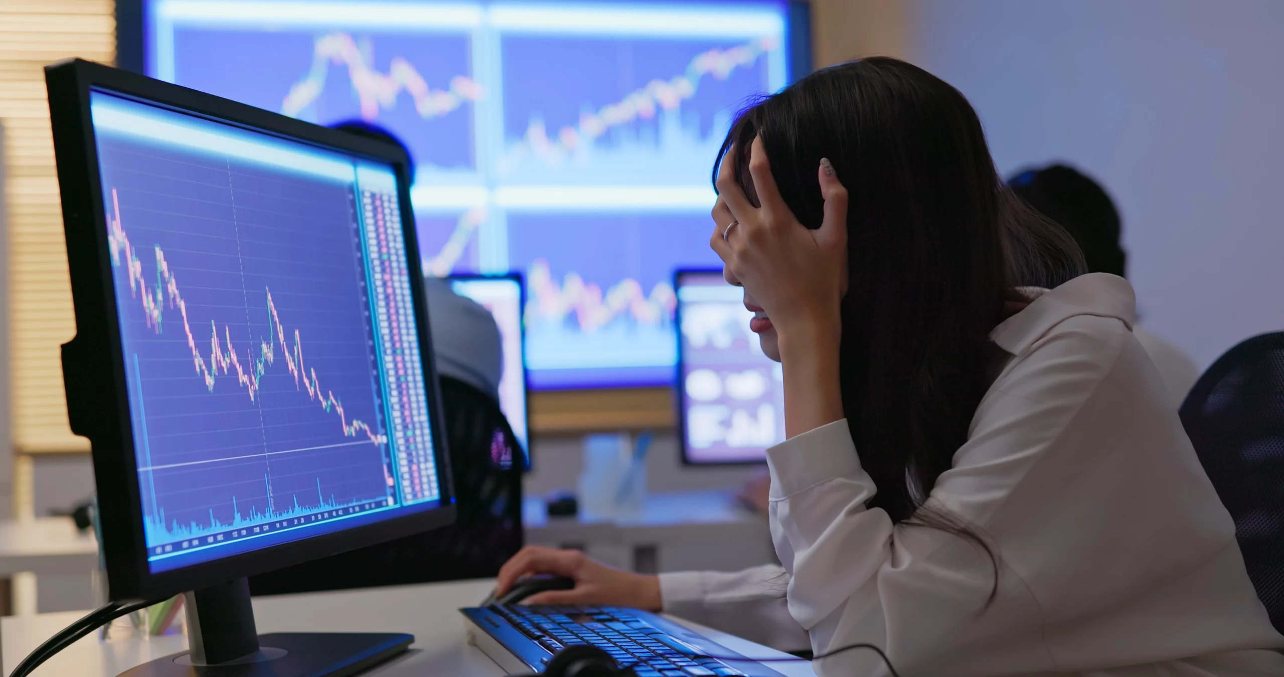 A woman holds her head in her hands as she watches a market crash on her computer
