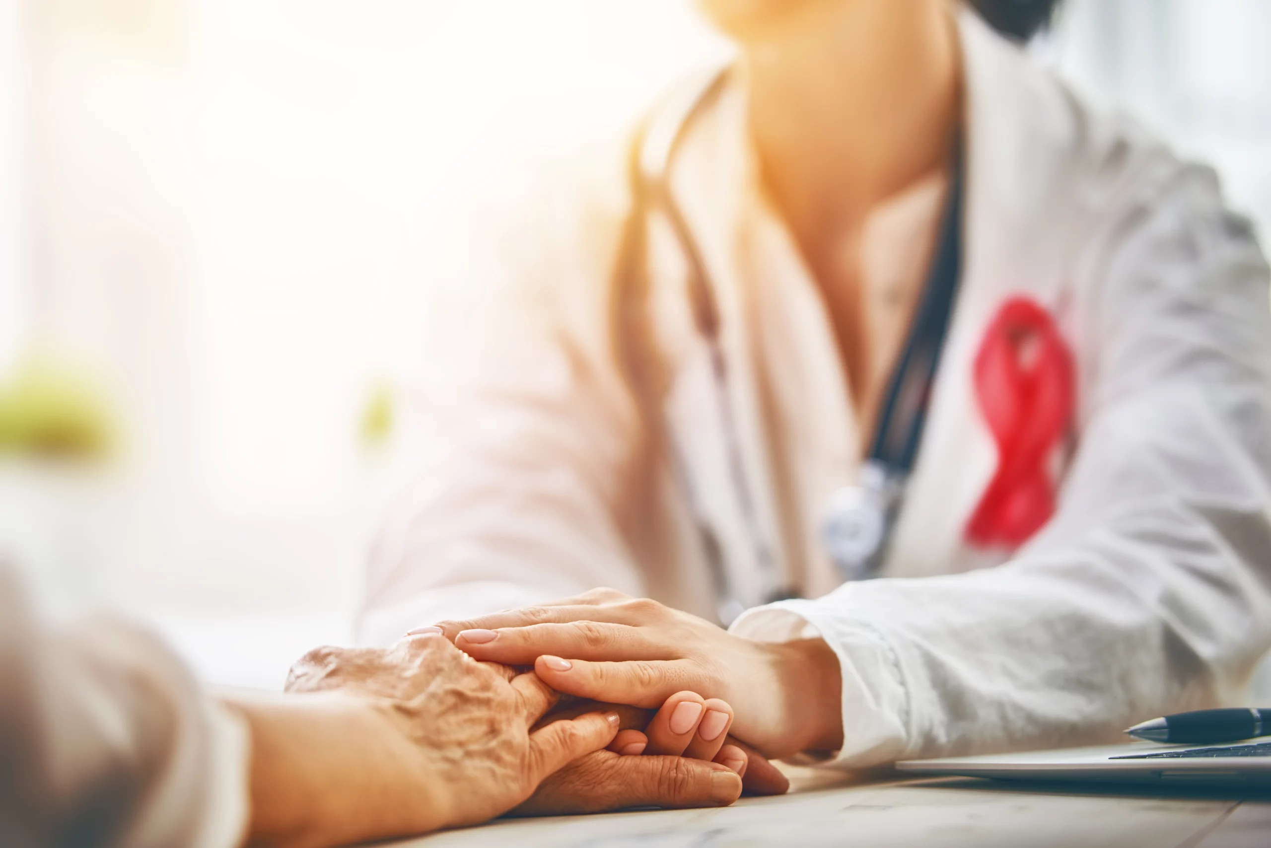 A healthcare provider wearing a cancer ribbon holds the hand of a patient