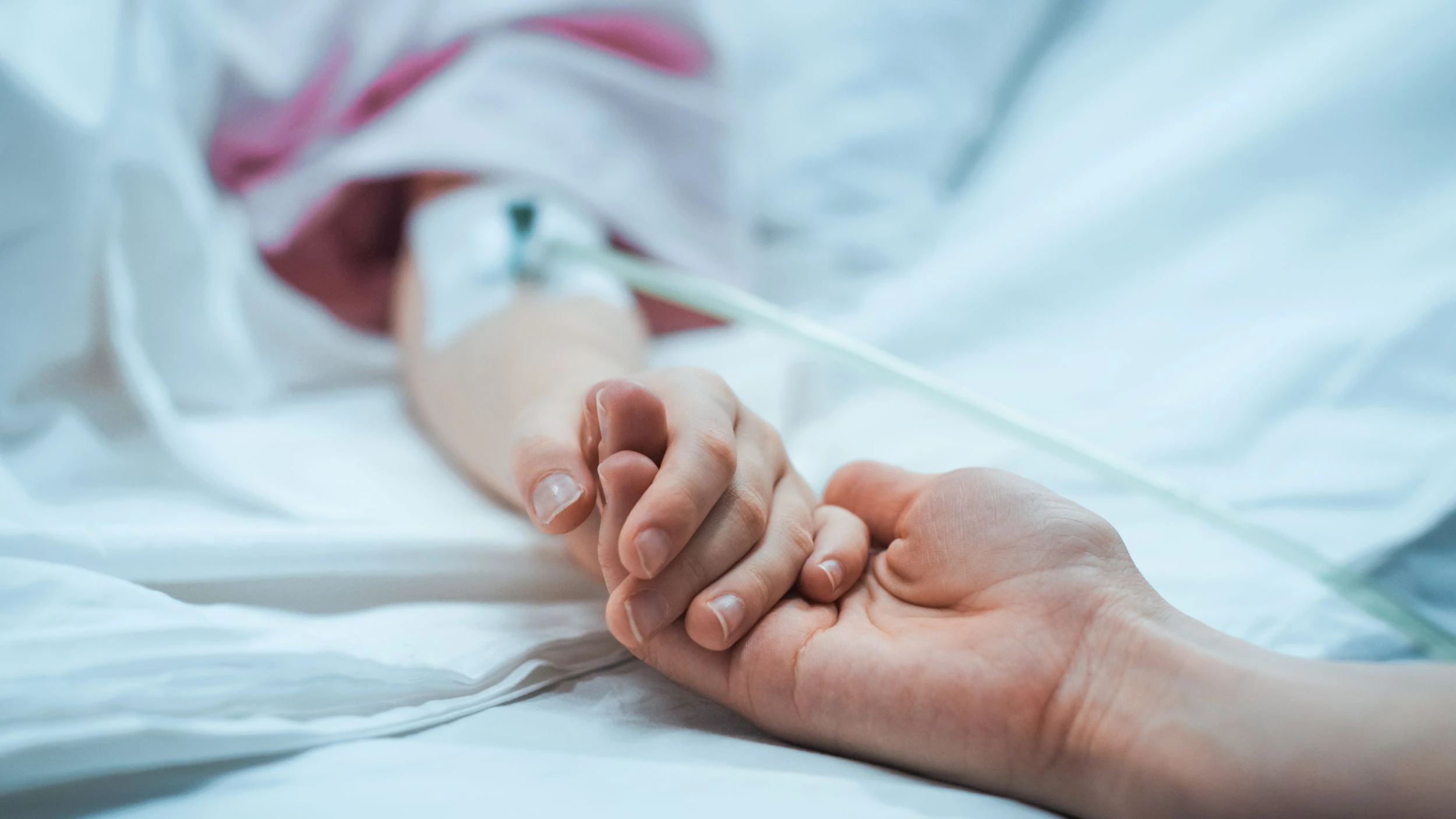 A parent holds the hand of a critically ill child