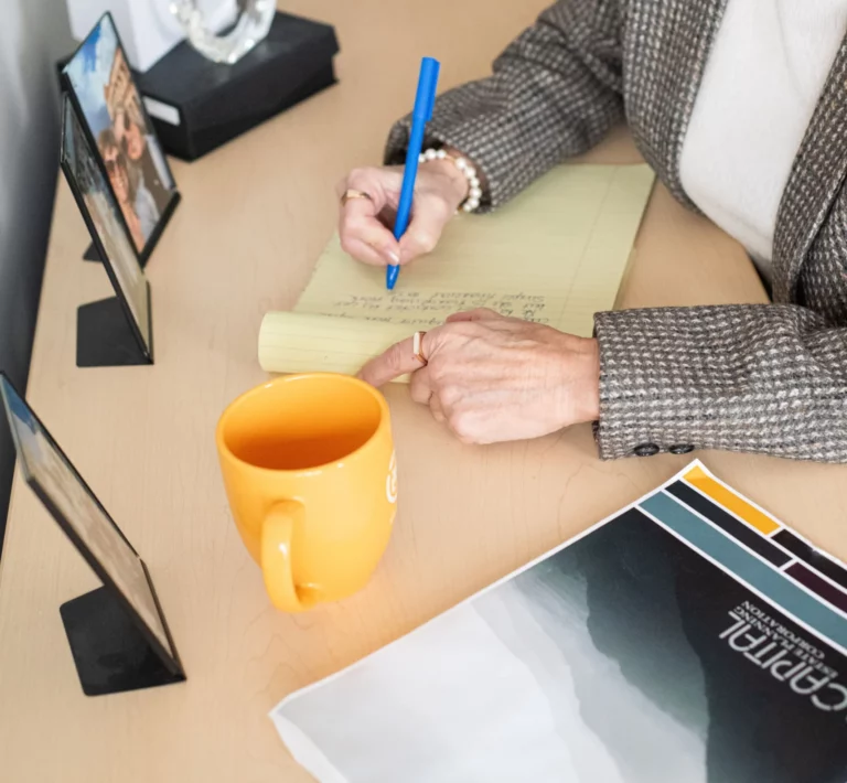 A woman sitting at a desk, writing on a notepad with a coffee mug nearby