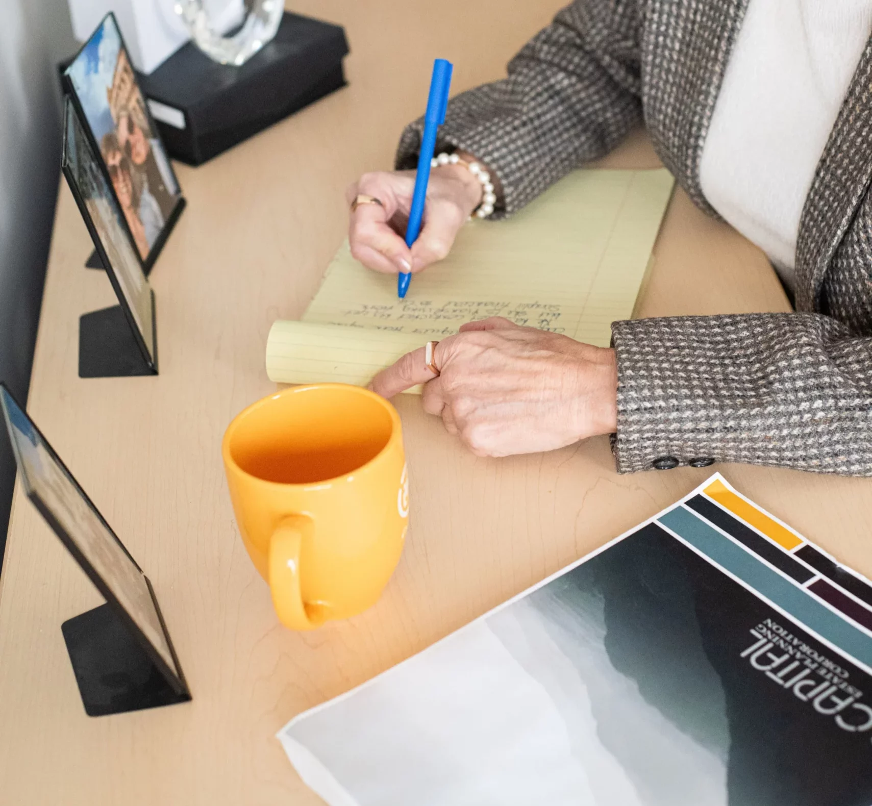 A woman sitting at a desk, writing on a notepad with a coffee mug nearby